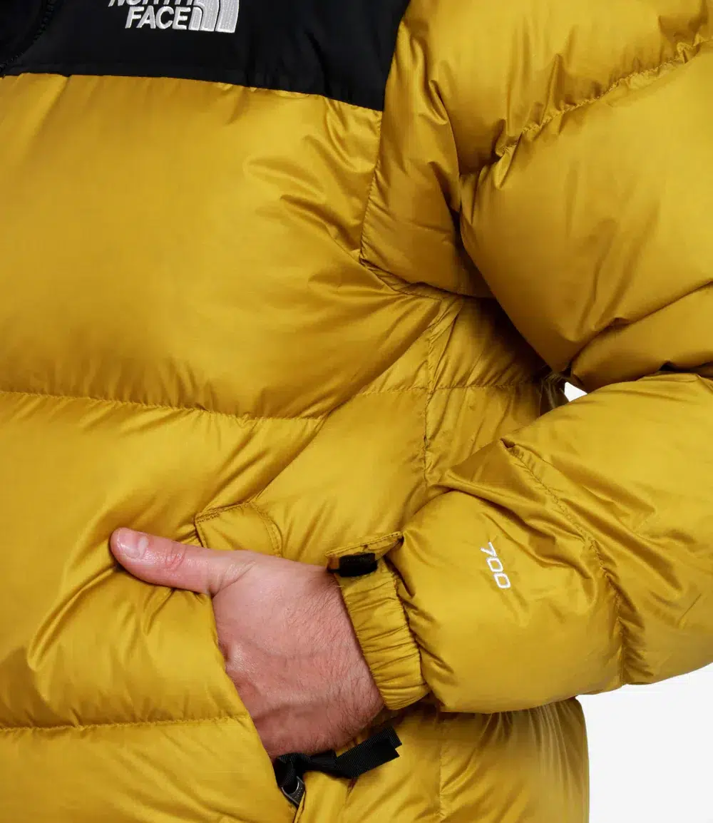 Eine Nahaufnahme einer Person, die eine gelbe The North Face-Pufferjacke trägt und eine Hand in der Jackentasche hat.
