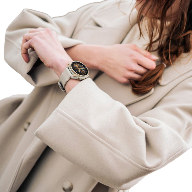 Une personne portant un manteau beige ajuste sa manche, laissant apparaître une montre-bracelet au cadran noir et or.
