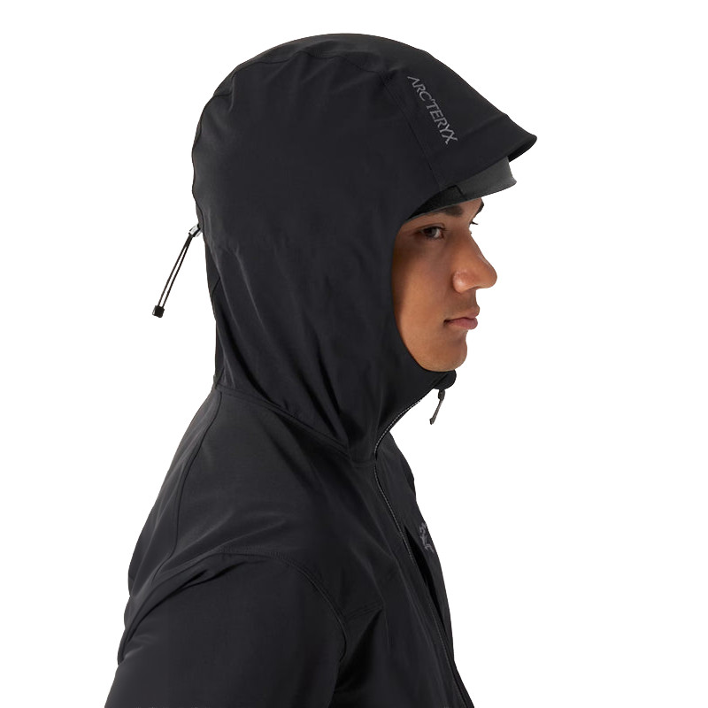Person, die eine schwarze Arc'teryx-Kapuzenjacke trägt, in der Profilansicht nach rechts, mit vollständig geöffneter Kapuze und sichtbarem Kordelzug am Rücken.